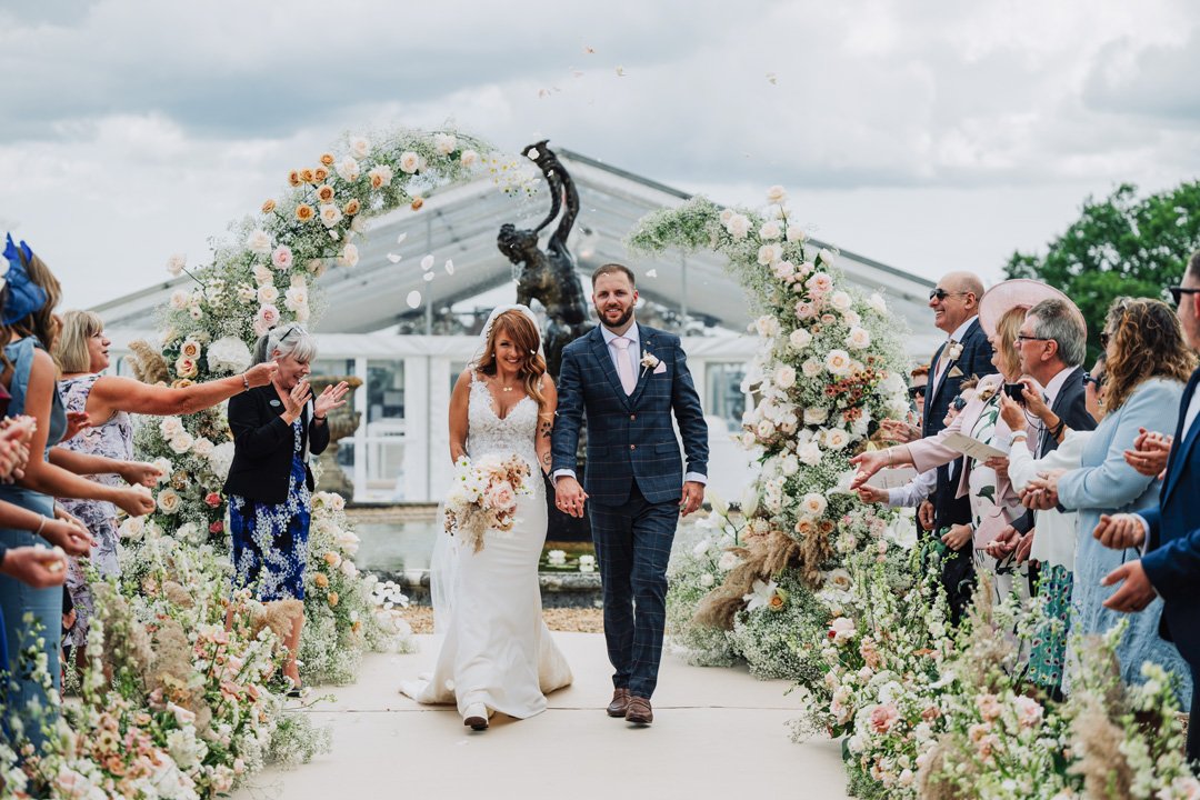 A Bride and Groom walk through a beautiful arrangement of fresh luxury wedding flowers.