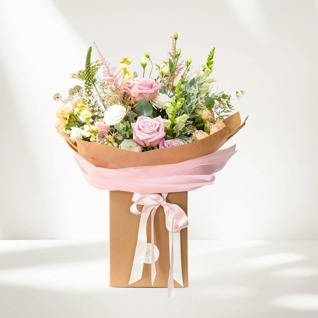 A bouquet of beautiful fresh flowers in a presentation box with ribbons and a gift tag.