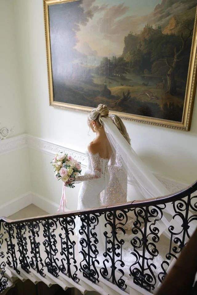 a bride descends a grand staircase carrying her stunning floral bouquet.