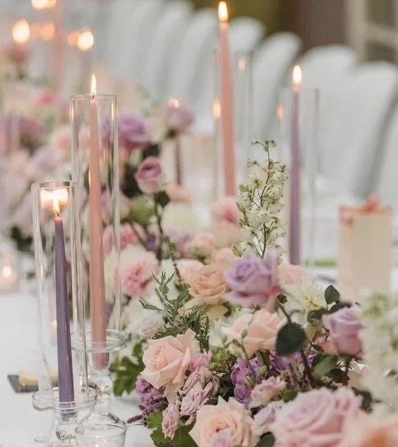 A wedding table decorated with beautiful pink and lilac flowers with lighted candles.