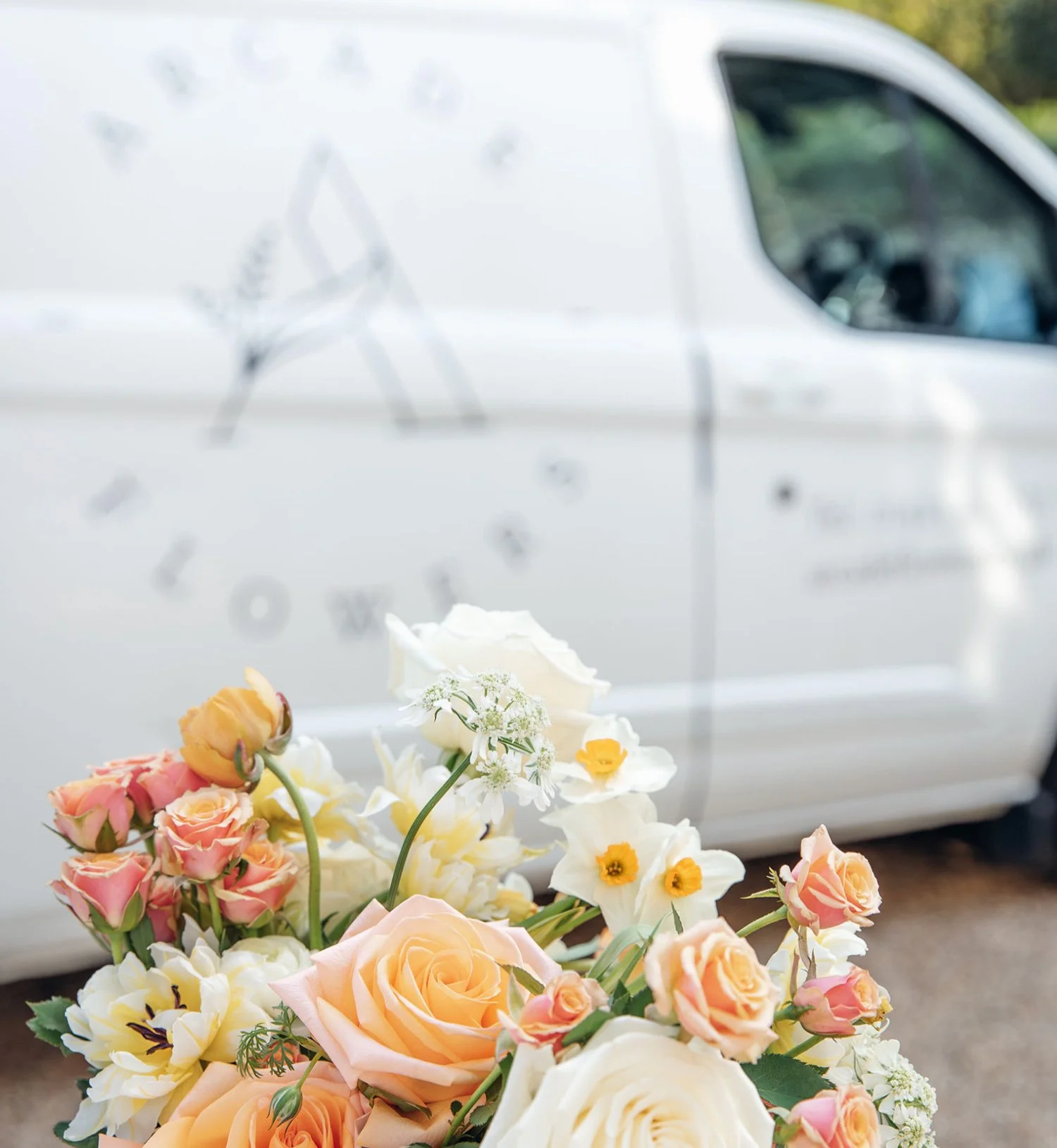 Colourful bouquet of roses and other flowers in front of the Arcade Flowers Delivery van. The vehicle is out of focus in the background.