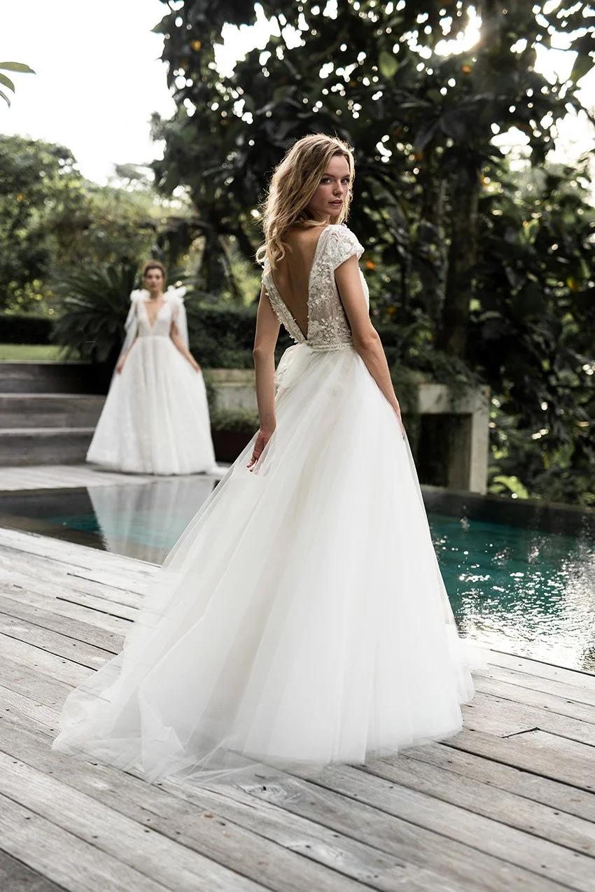 Woman wearing a tulle ballgown with V Neckline and fully embroidered lace top "Avery" by Atelier Edwin Oudshoorn standing by a swimming pool