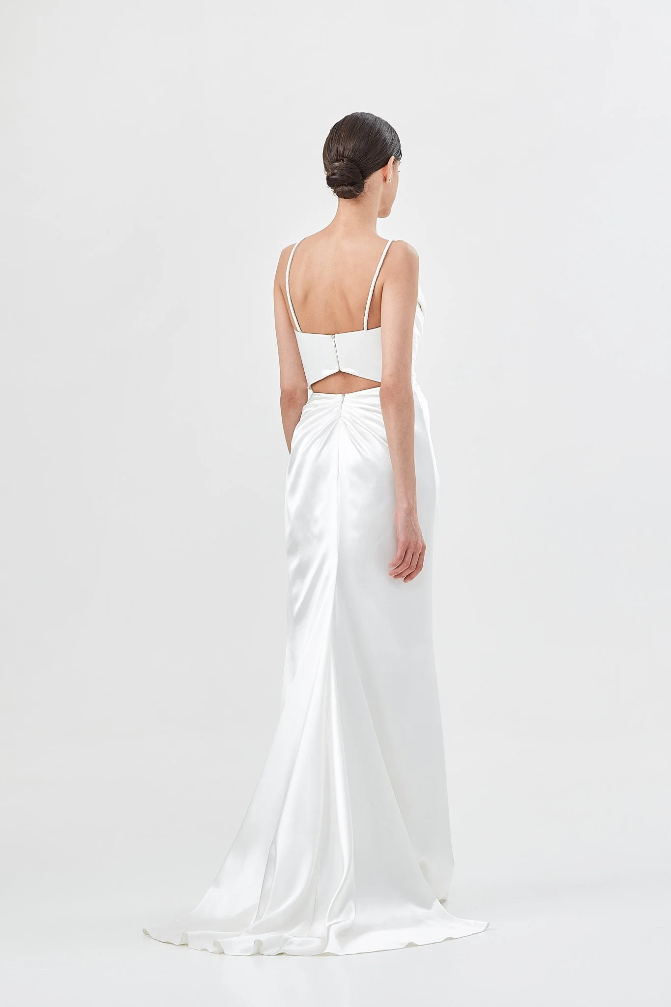 Woman wears strapless wedding dress made from bias cut silk satin with draped corset and skirt in a white photo studio