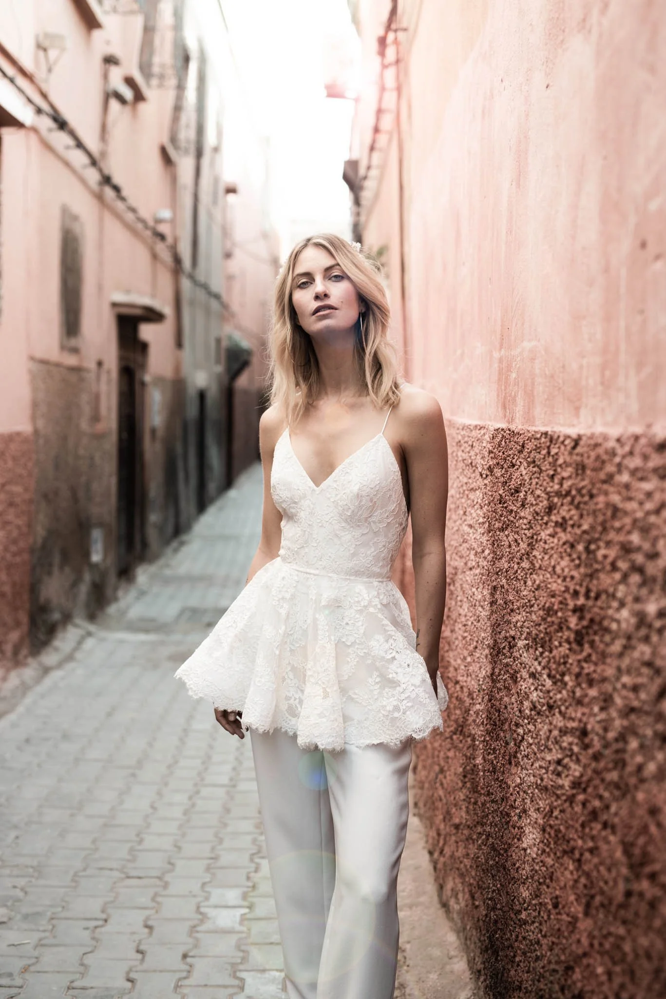 Bride wearing an Edwin Oudshoorn Lace jumpsuit with peplum top leaning against a wall in Marrakech