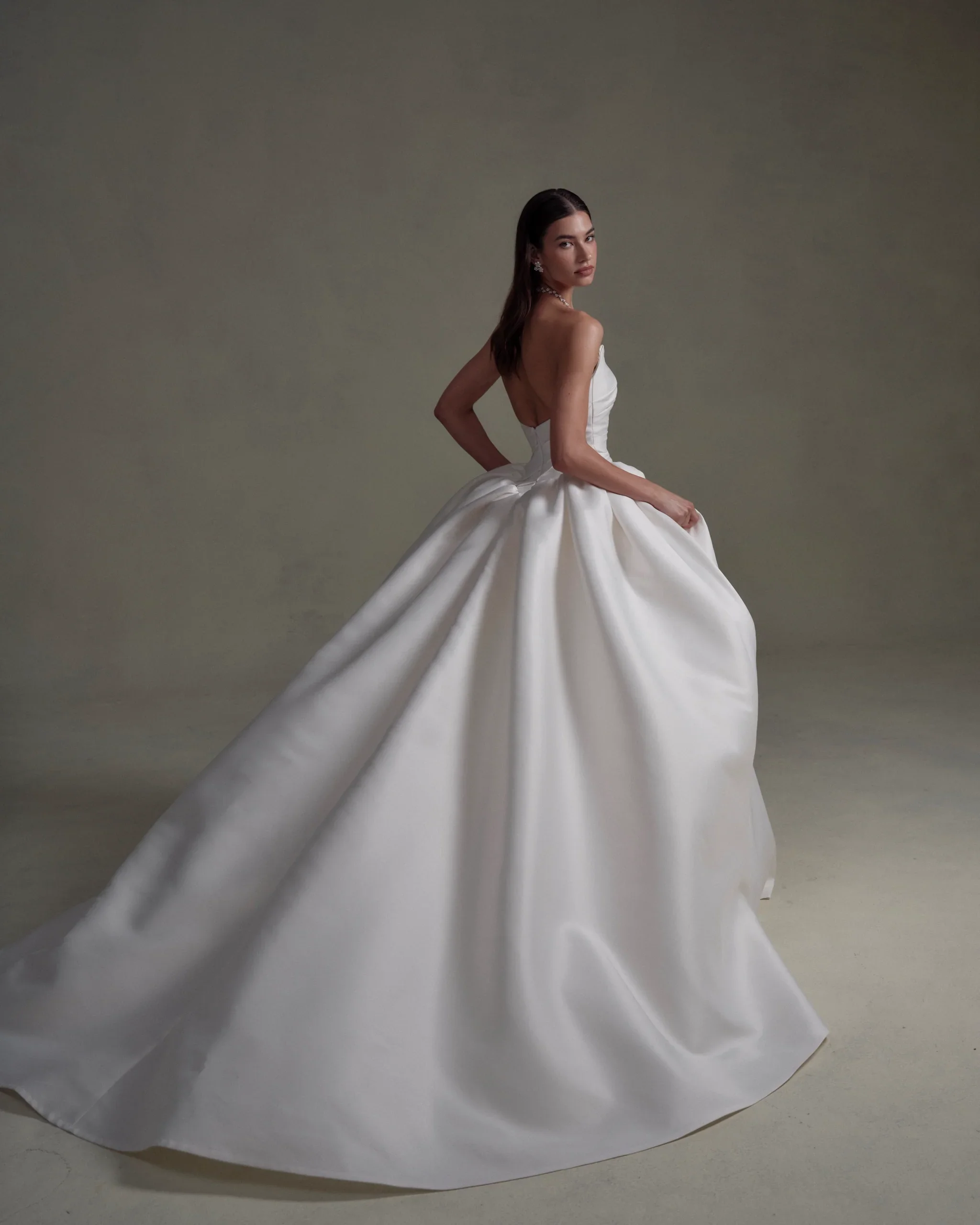 A woman in a strapless white wedding gown with a full, flowing skirt, standing against a plain background.