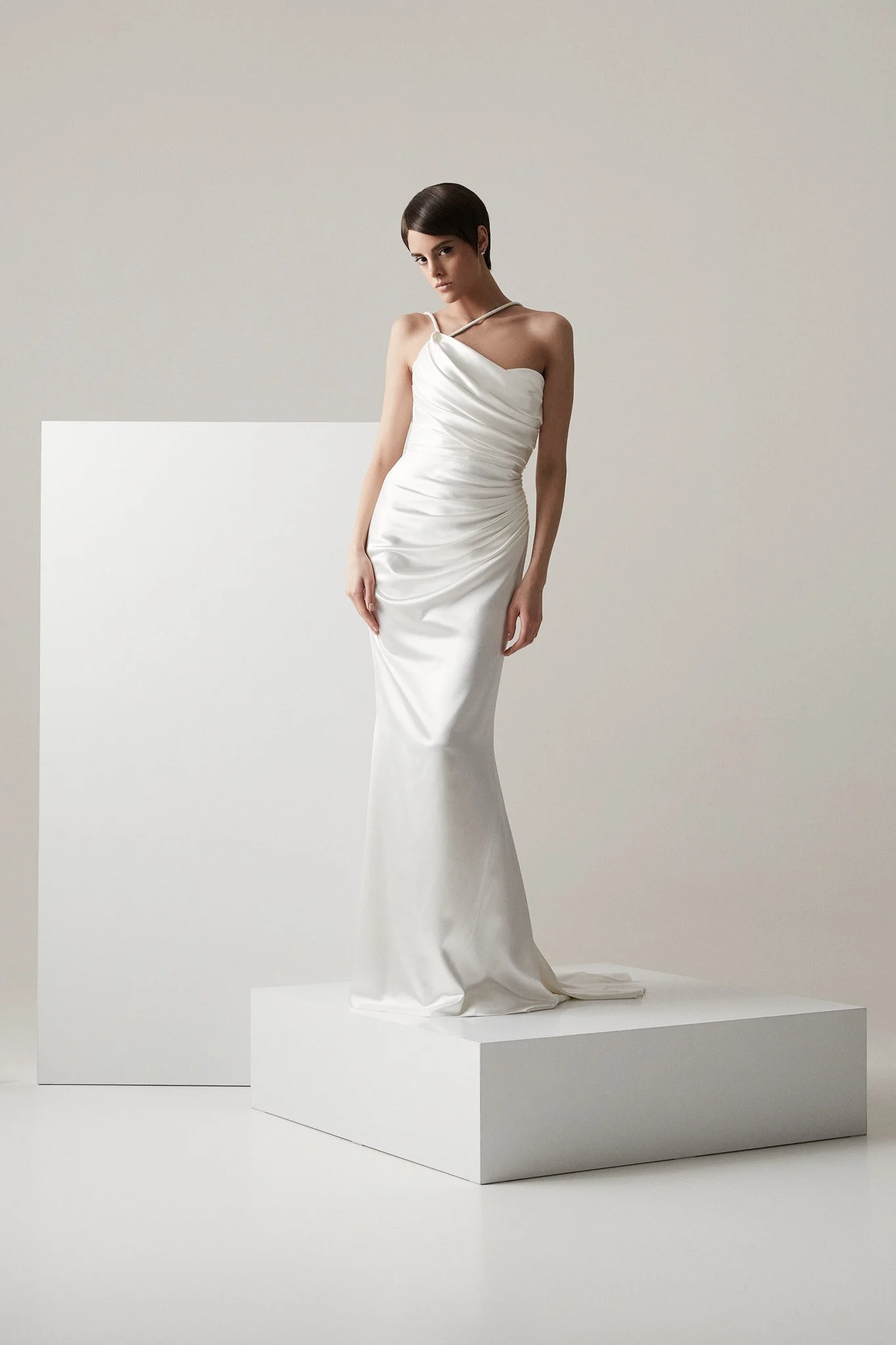 Woman wears strapless wedding dress made from bias cut silk satin with draped corset and skirt in a white photo studio