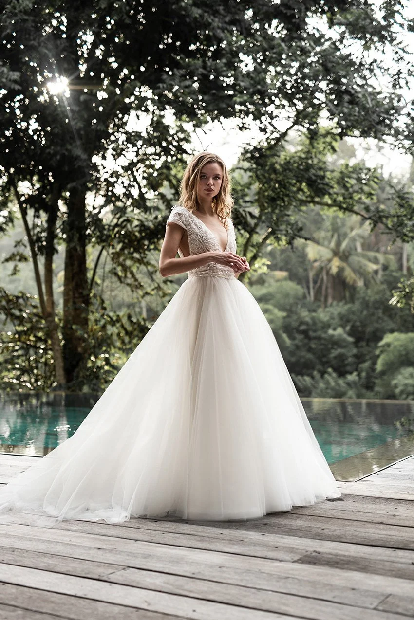 Woman wearing a tulle ballgown with V Neckline and fully embroidered lace top "Avery" by Atelier Edwin Oudshoorn standing by a swimming pool