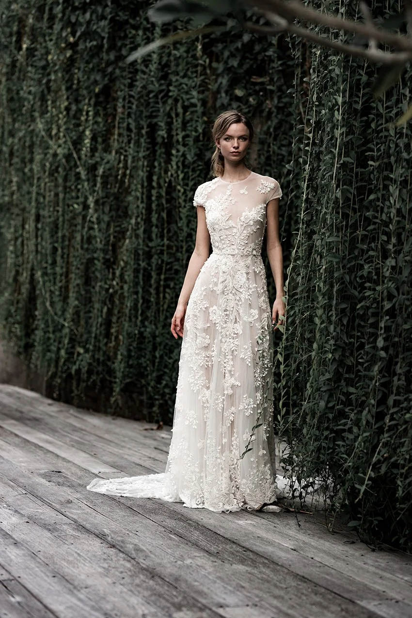 Woman in fully beaded floor length bridal gown standing against a living green wall