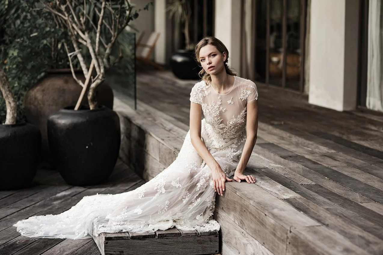 Woman in fully beaded floor length bridal gown sitting on a wooden deck
