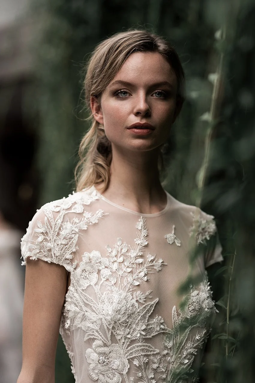 Woman in fully beaded floor length bridal gown standing against a living green wall
