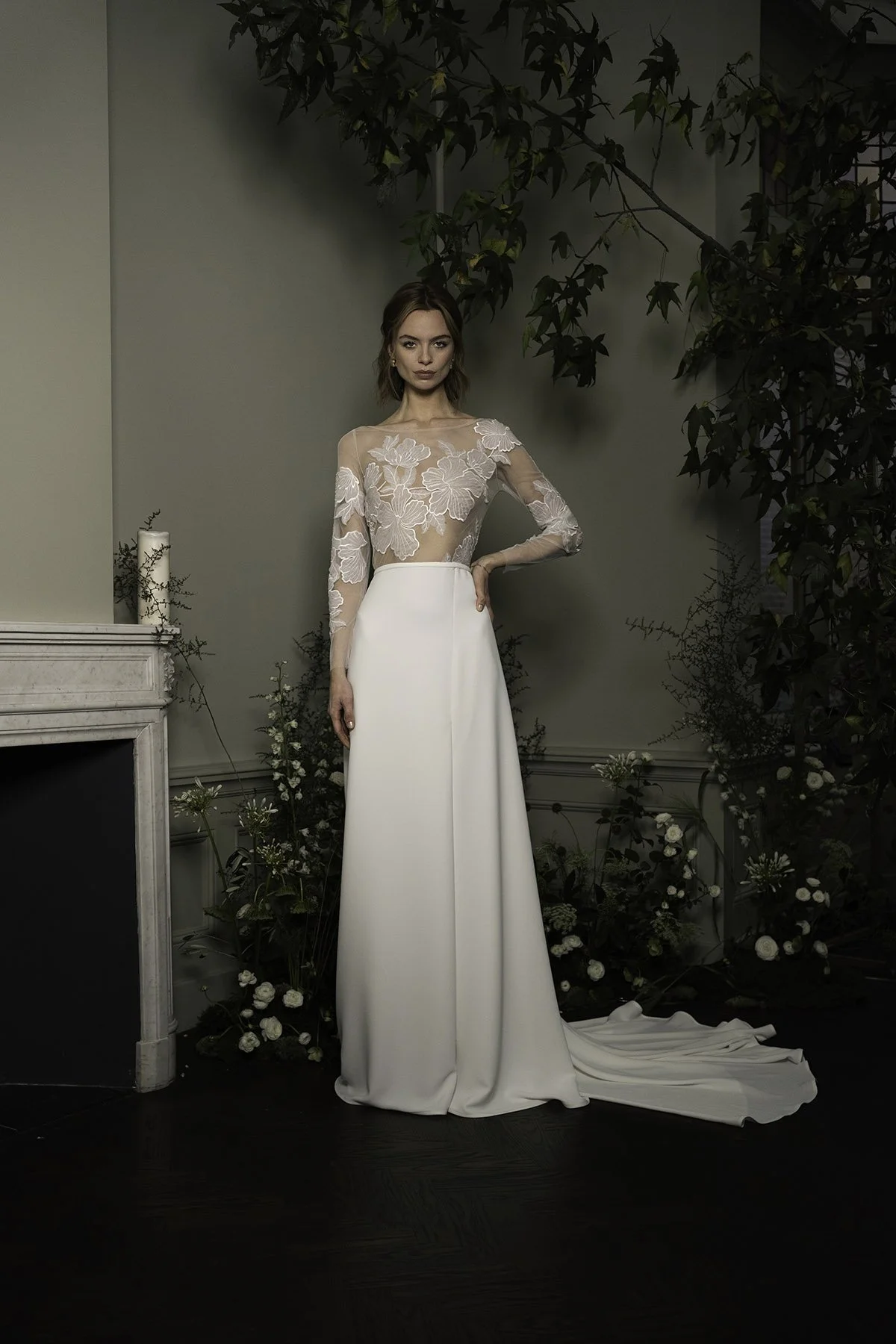 Woman wearing a wedding gown with long sleeves, a lace top with large flowers, a white crepe skirt,