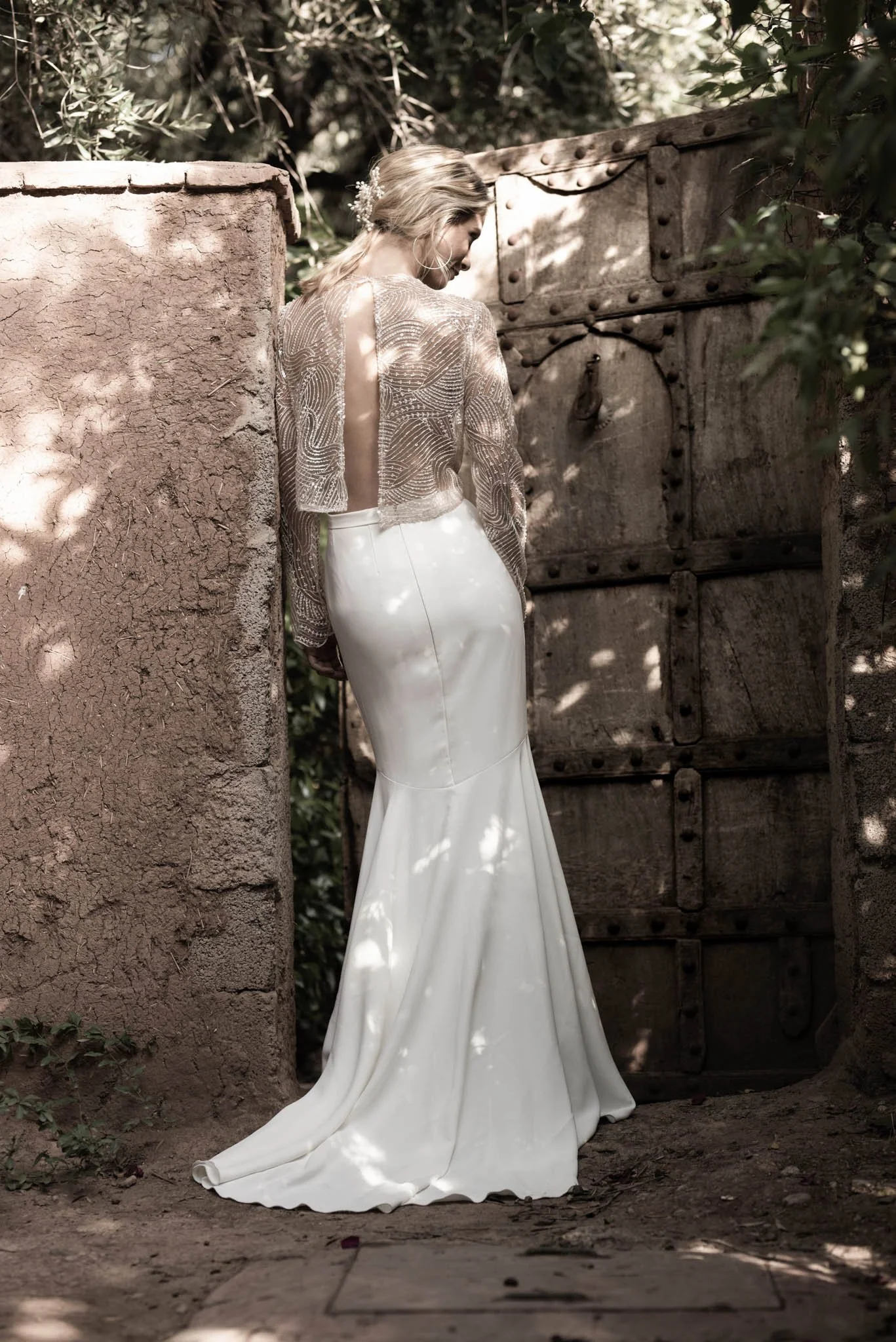 Bride wears wedding dress with embroidered tulle top with open back and crepe fishtail skirt, posing in Marrakech