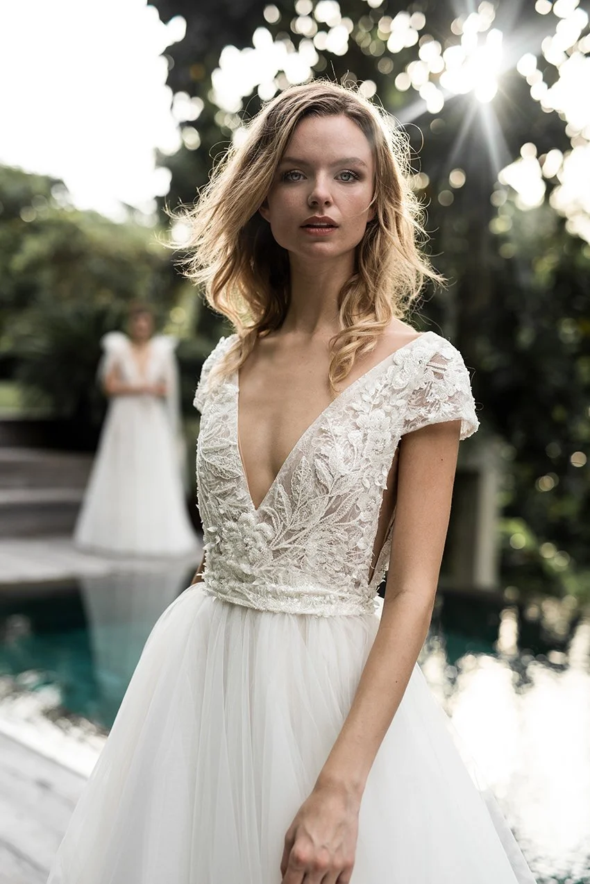 Woman wearing a tulle ballgown with V Neckline and fully embroidered lace top "Avery" by Atelier Edwin Oudshoorn standing by a swimming pool