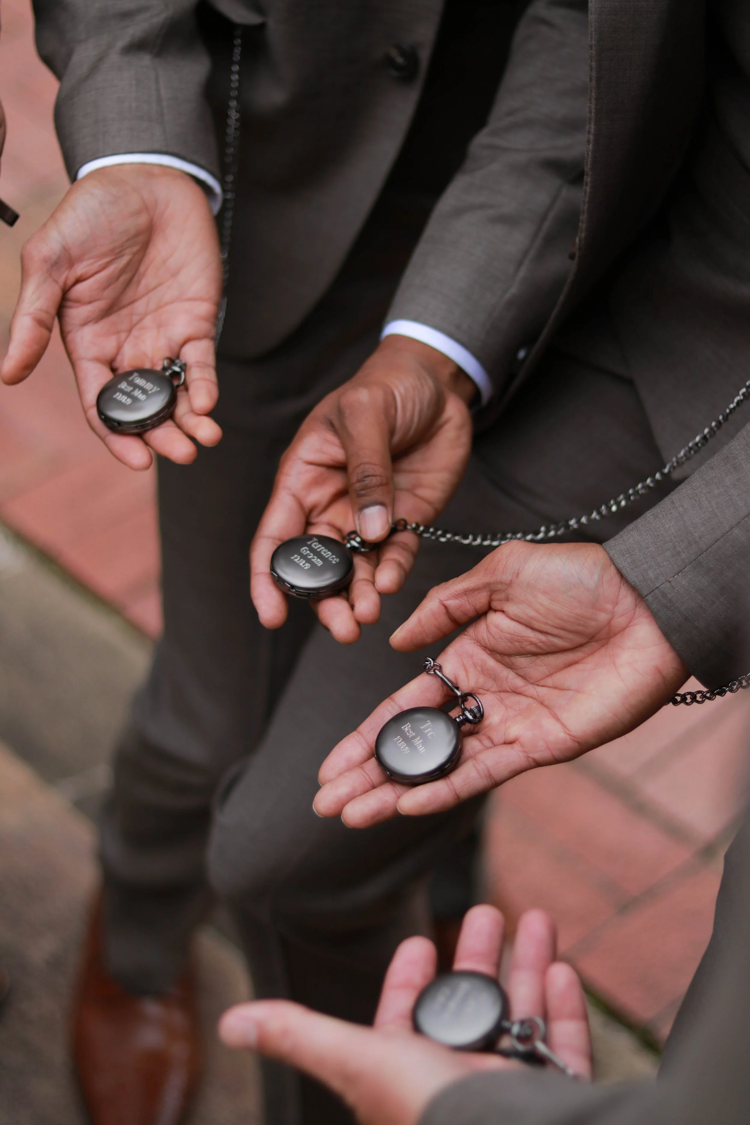 Four people dressed in suits are holding black pocket watch necklaces with engraved messages on them.
