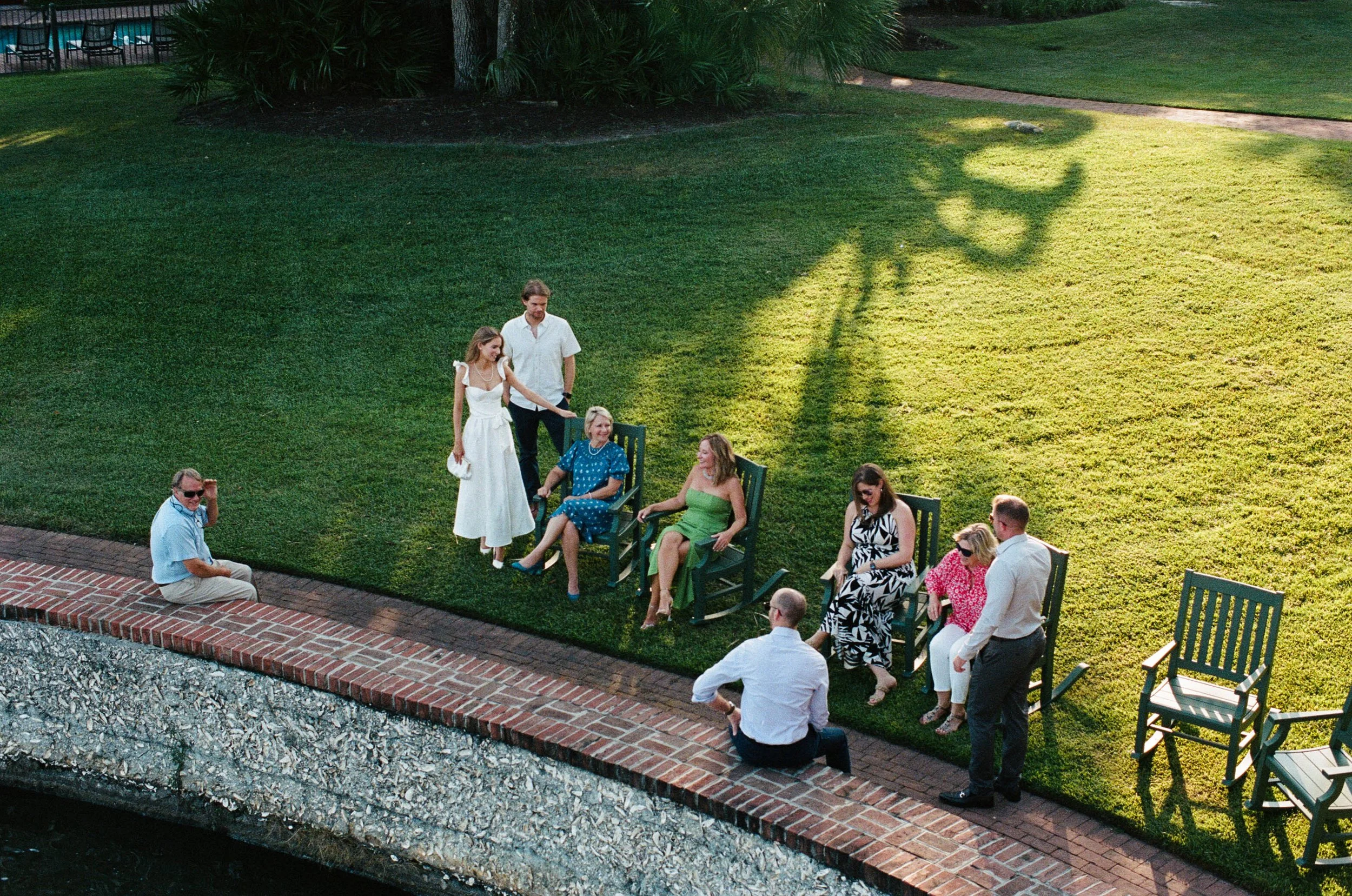 Group of people relaxing on lawn chairs near a brick path in a garden setting during the day.