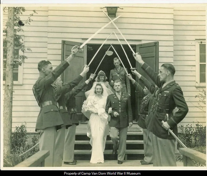 Photograph of Captain and Mrs. Adelbert Dale Boggs as they leave Camp Van Dorn Chapel where they were married on April 11, 1943. Six Soldiers hold their swords over the couple as they exit the Chapel in a salute to the couple.