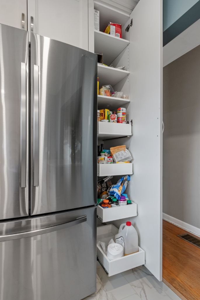 Slim pull-out pantry cabinet beside a refrigerator providing organized vertical storage for pantry items.