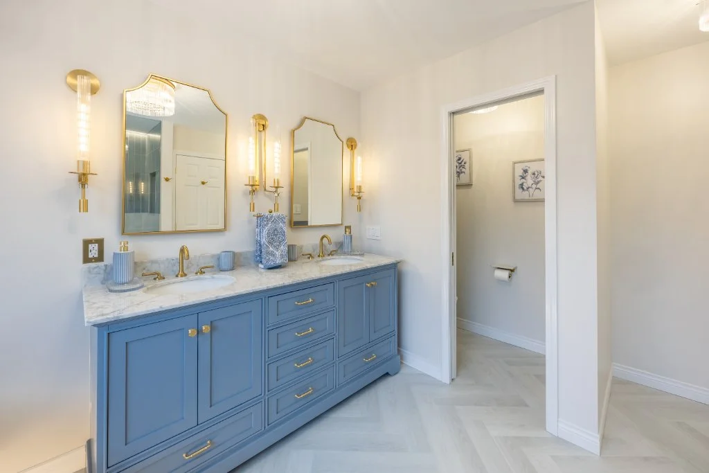 Sky-blue double vanity with marble countertop, gold hardware, decorative mirrors, and designer lighting in a custom ensuite renovation.