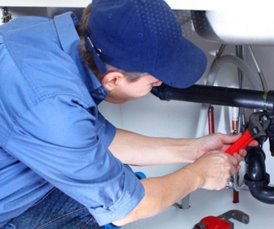 Plumber in blue uniform using a wrench to repair piping under a sink—illustrating hands-on renovation problem-solving.