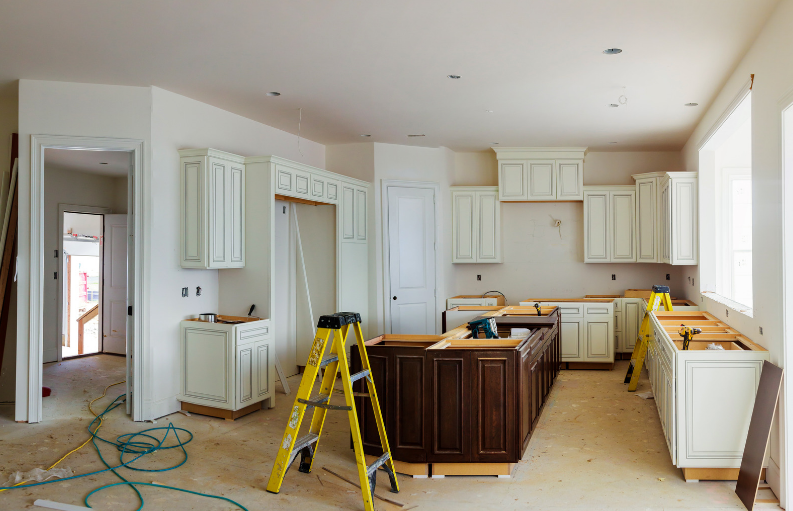Kitchen renovation in progress with partially installed cabinets, a large island and construction ladders.