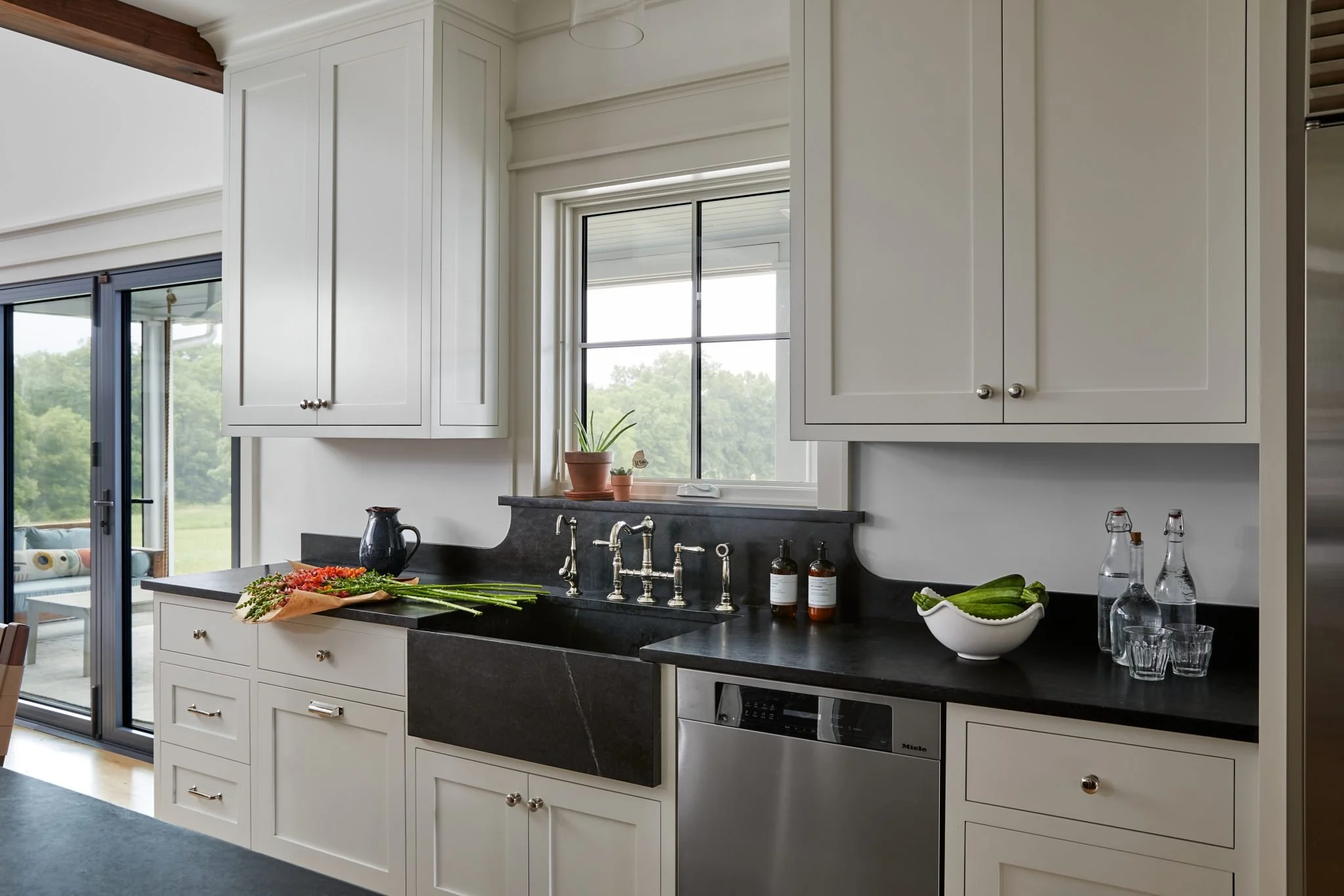 Kitchen renovation featuring dark soapstone countertops, farmhouse sink and white shaker cabinets with modern hardware