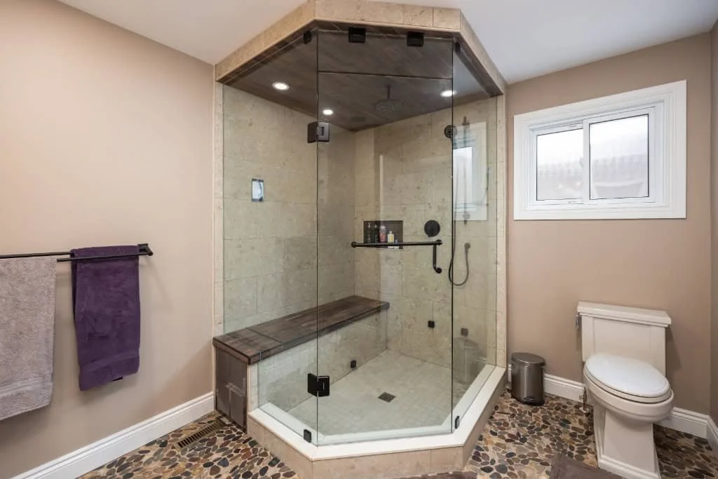 Glass-enclosed corner shower with a built-in bench, handheld showerhead and tiled shower floor.
