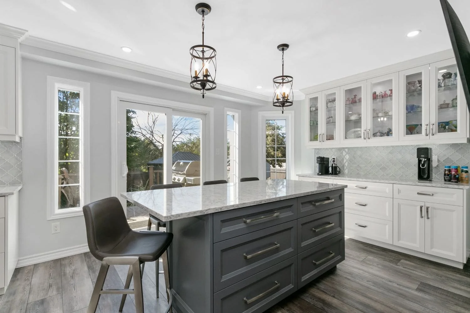 Large dark grey kitchen island with storage drawers, seating and pendant lights in a bright white kitchen