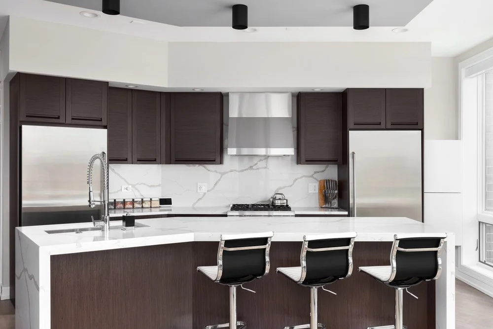Contemporary kitchen with a white quartz waterfall countertop on a peninsula and matching quartz backsplash.