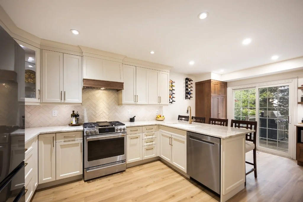 Custom kitchen renovation featuring an L-shaped layout with white shaker cabinets, quartz countertops, stainless steel appliances, and peninsula seating designed for both cooking and entertaining.