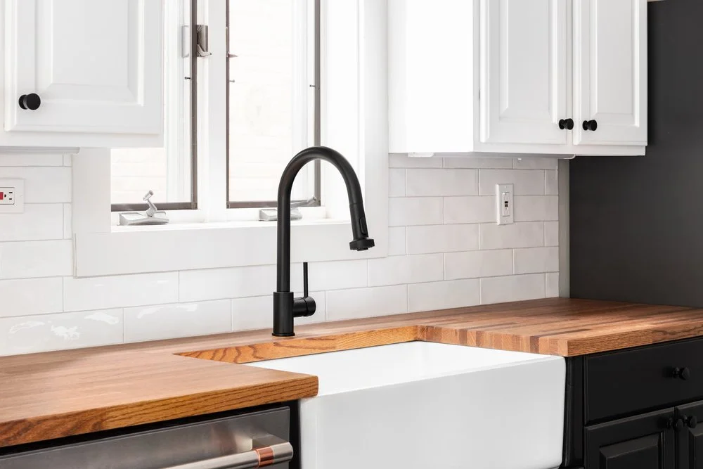 Kitchen featuring butcher block countertops with farmhouse apron sink, white subway tile backsplash and black cabinetry accents