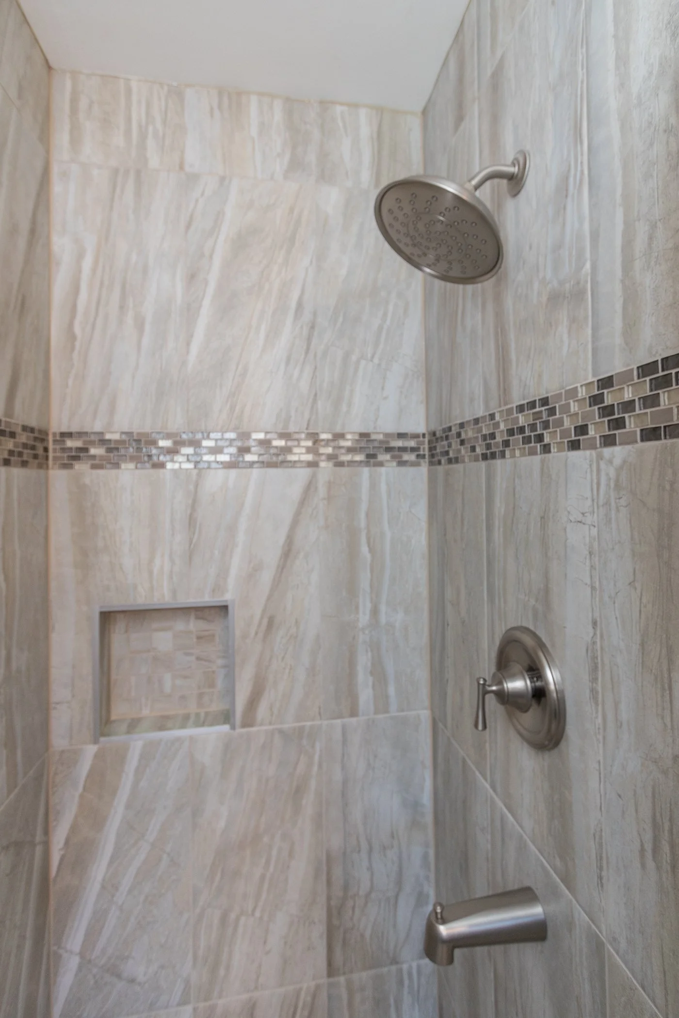 Large-format porcelain tile shower featuring a decorative accent strip, recessed niche and frameless glass enclosure.
