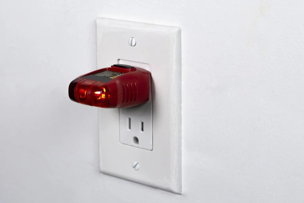 Receptacle tester is plugged into a decora receptacle to test its polarity and to see if it's wired corrected. Two lights are lit up on the right which indicates it's correct.
