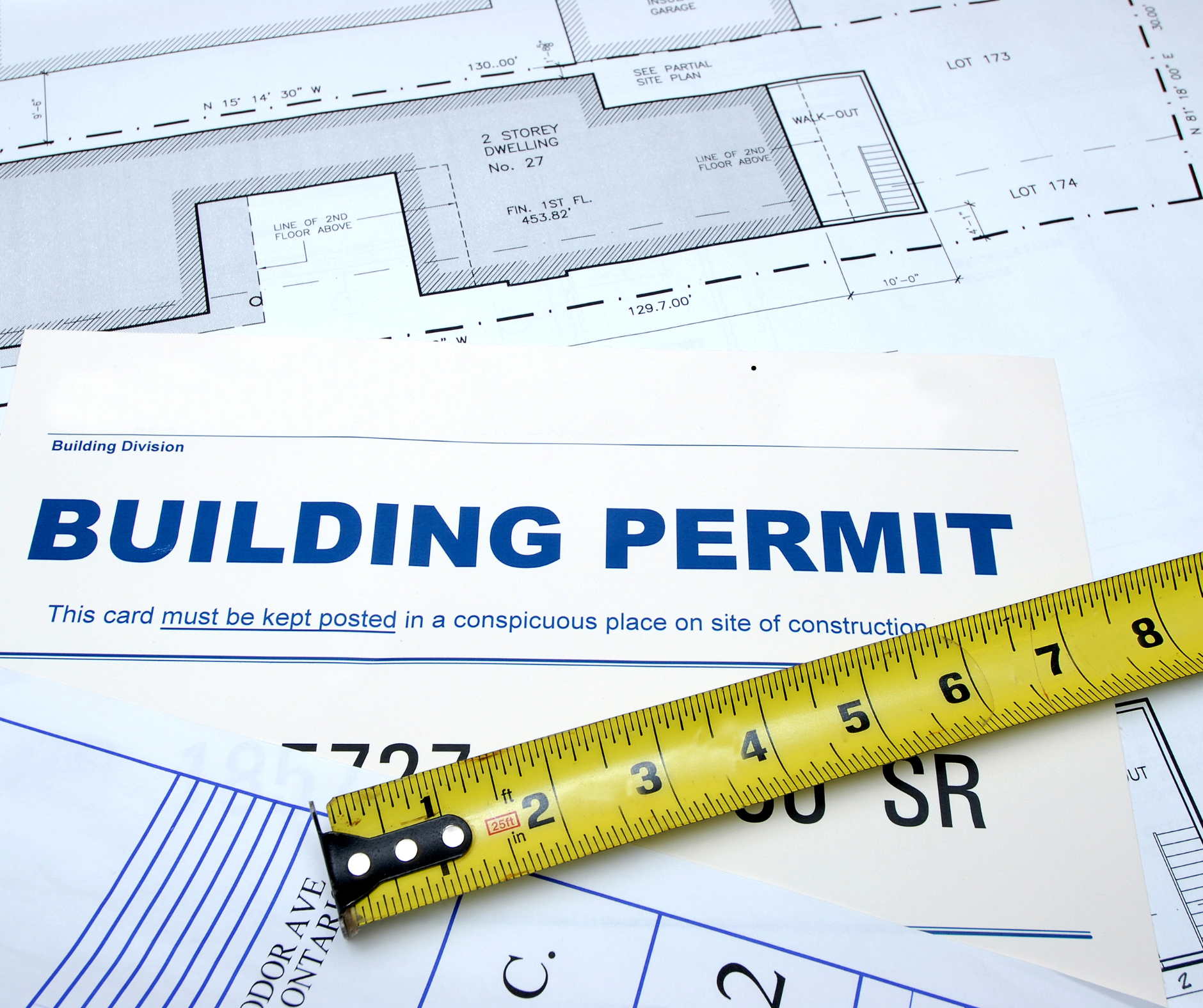Building permit paperwork, renovation drawings, and measuring tape representing the permit and planning stage of a home renovation project.
