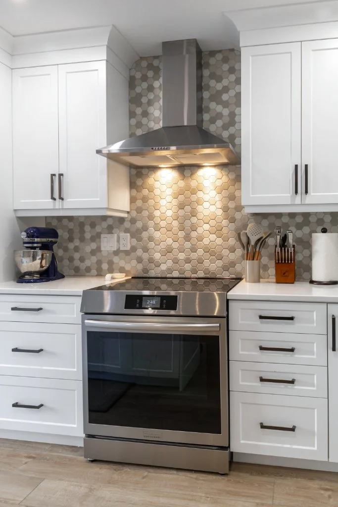 Kitchen renovation featuring white shaker cabinets, stainless steel range hood, hexagon tile backsplash, and custom cabinetry storage.