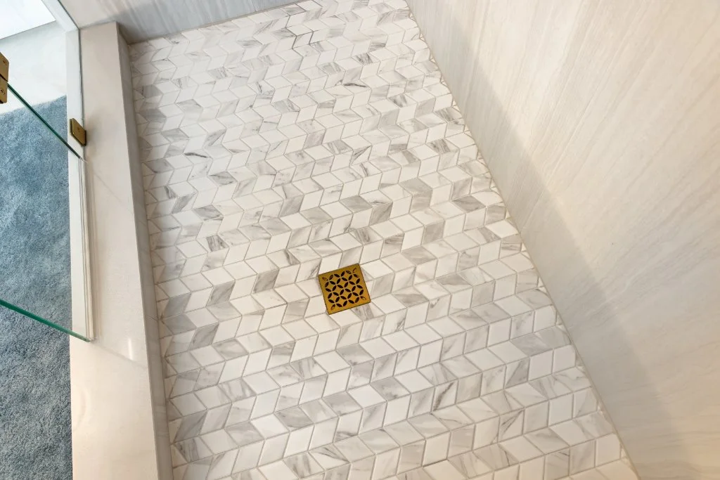 Custom shower floor featuring decorative mosaic tile and gold drain in a luxury ensuite bathroom renovation.
