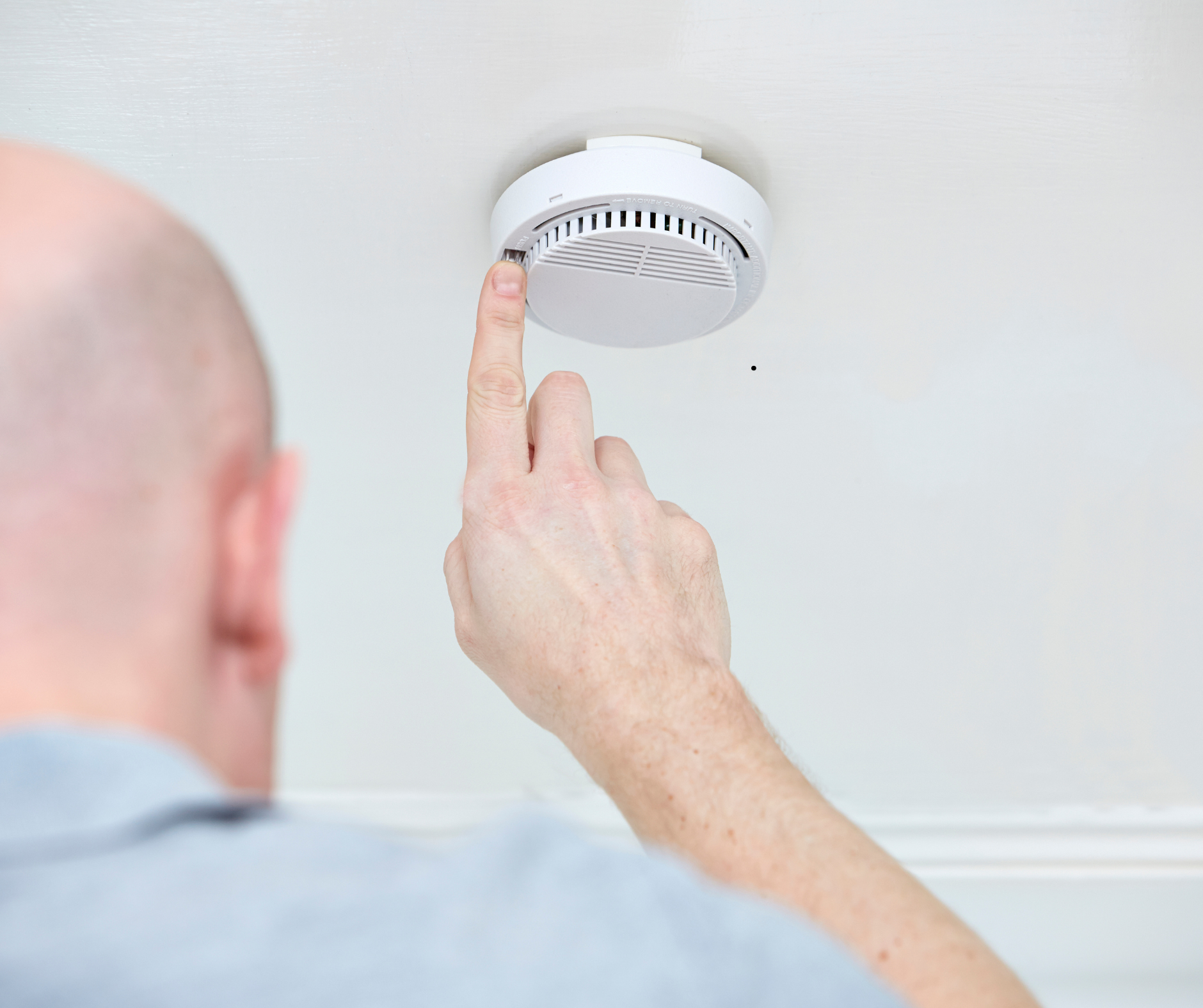 Person pressing the test button on a ceiling-mounted smoke detector to ensure it’s functioning properly.