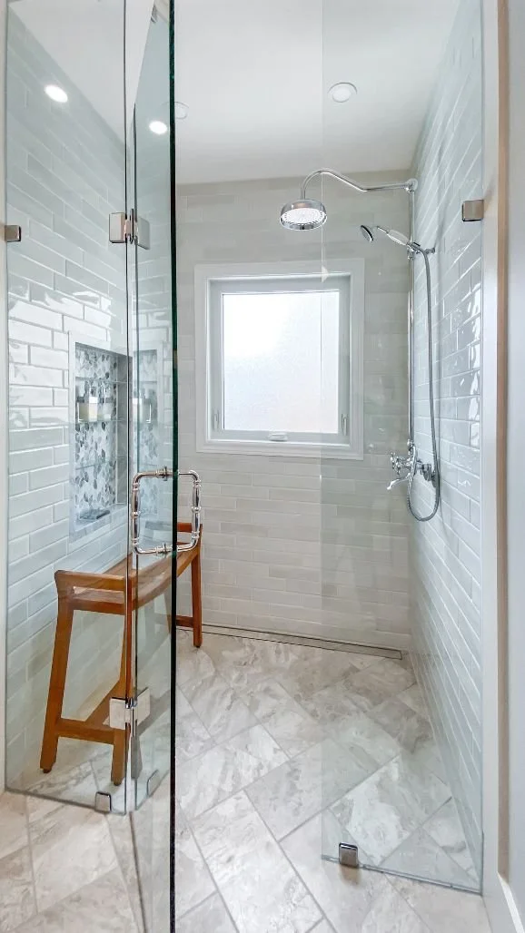 Walk-in shower finished with classic white subway tile, frameless glass enclosure and built-in shower niche.