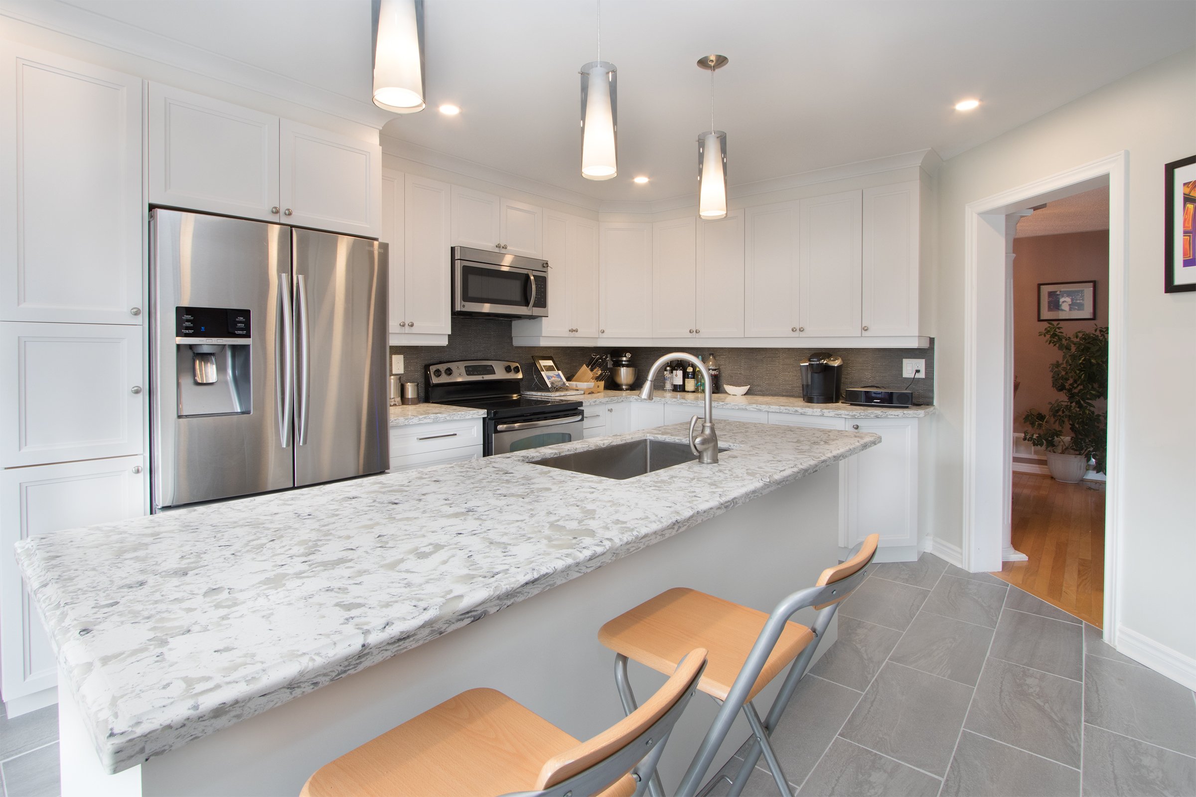White kitchen with a large island, sink, seating and pendant lighting.