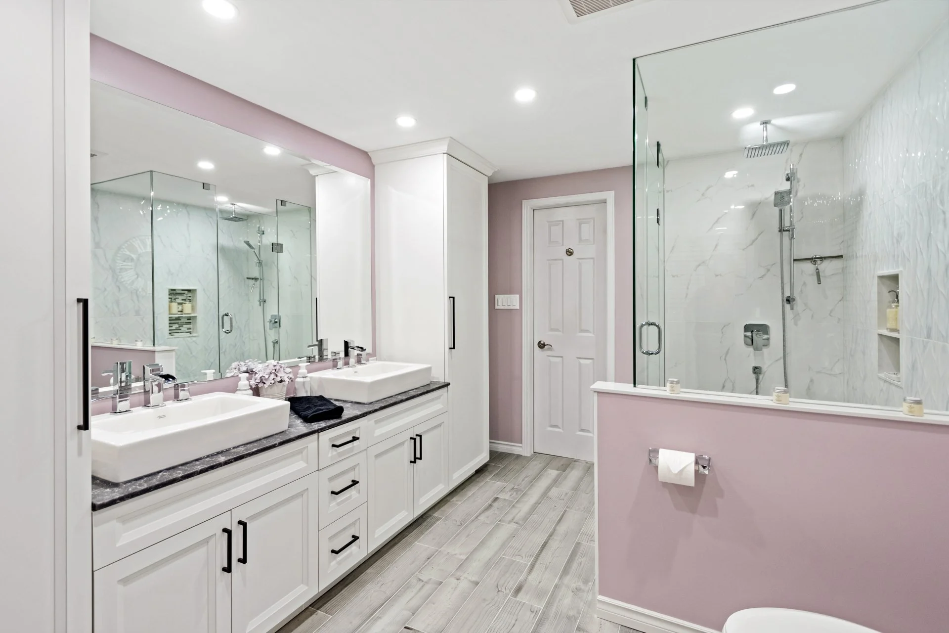 White double sink vanity with vessel sinks, black hardware and a large wall mirror in a renovated bathroom.