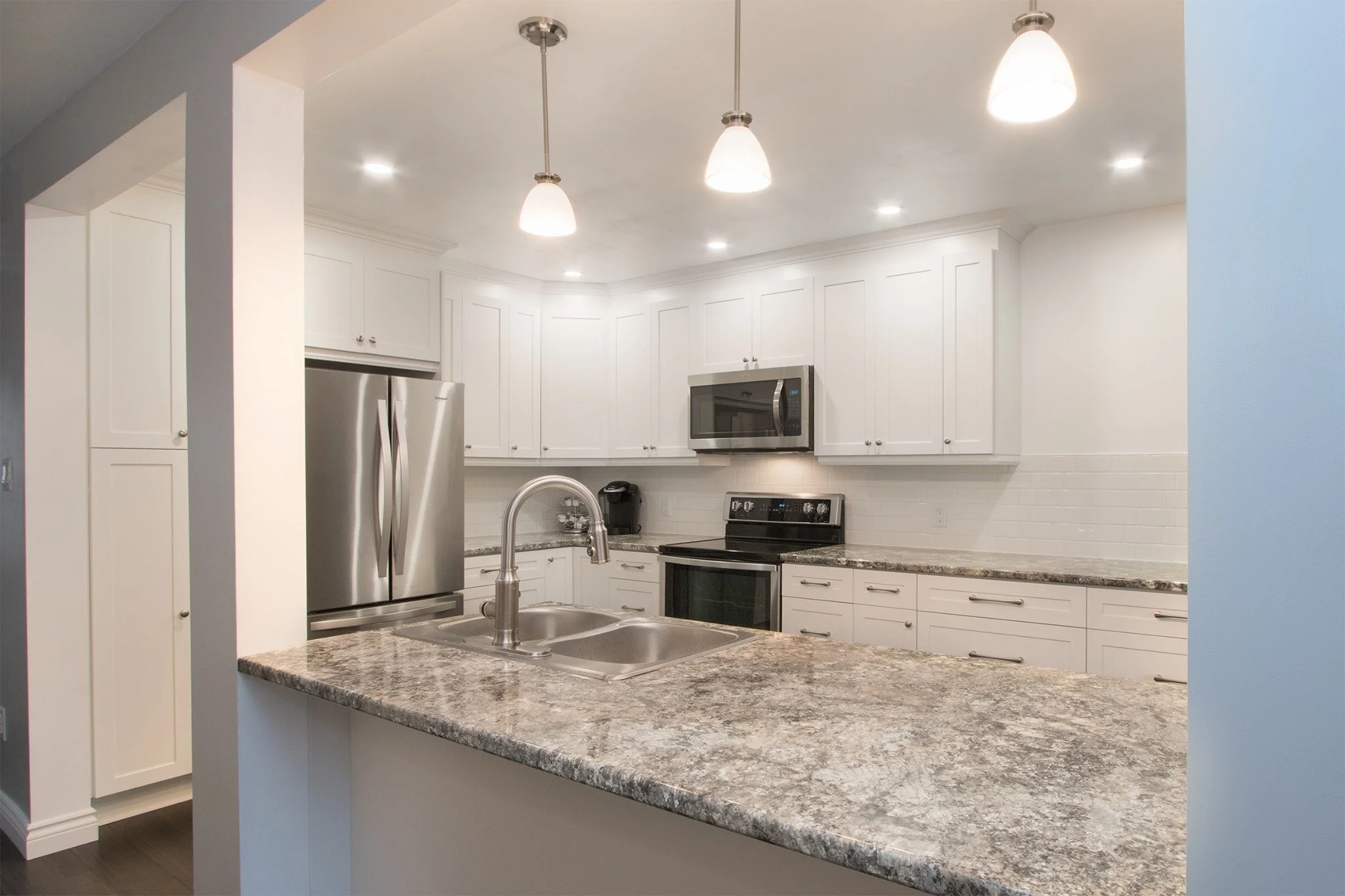 White kitchen renovation featuring laminite countertops, stainless steel appliances and pendant lighting over peninsula
