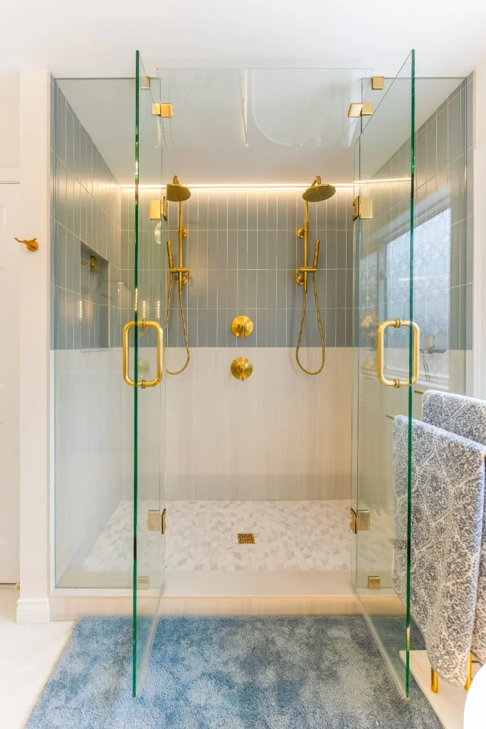 Custom walk-in shower with dual shower heads, dual controls, gold fixtures, frameless glass enclosure, and ceiling-height glass panels.