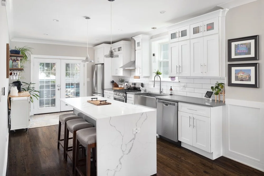White shaker kitchen with a quartz waterfall island and stainless steel appliances.