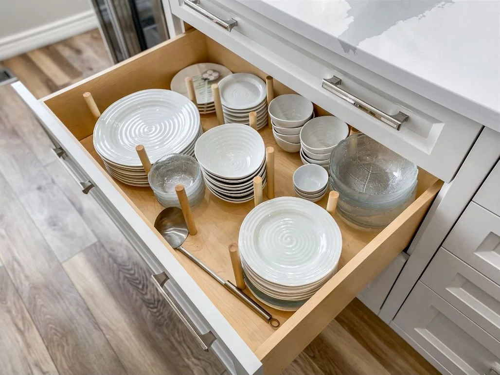 Deep kitchen drawer with organized plates, bowls and dishes using wooden pegs and adjustable dividers.