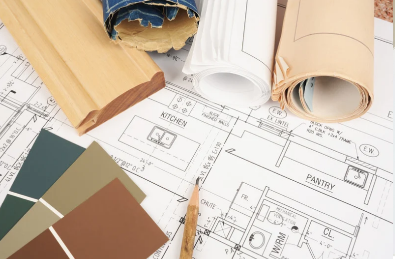 Kitchen renovation plans with architectural drawings, material samples and wood trim pieces spread across a work surface.