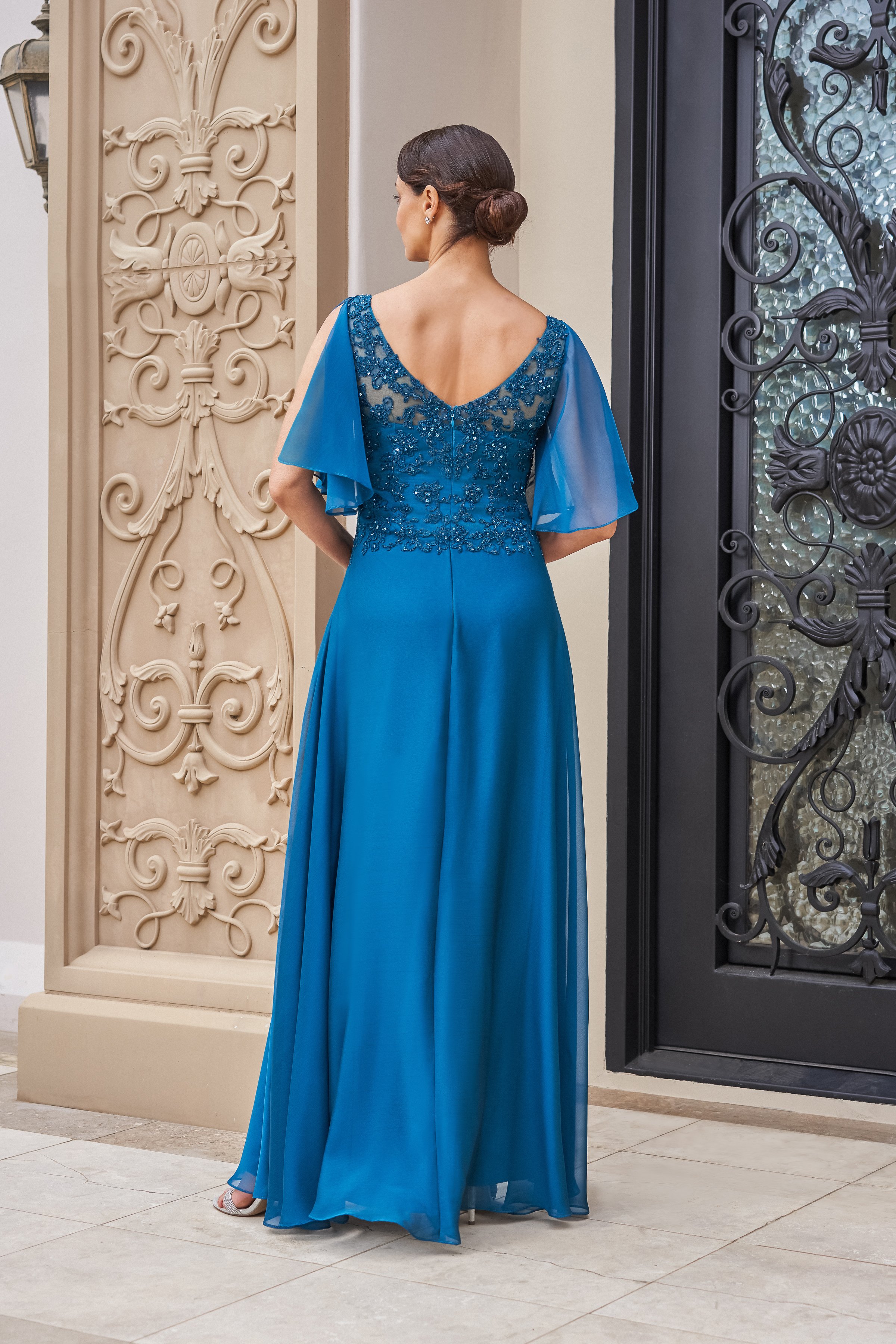Back view of a teal mother of the bride gown with a beaded lace V-back bodice, sheer flutter sleeves, and a flowing chiffon skirt designed for weddings and formal celebrations.