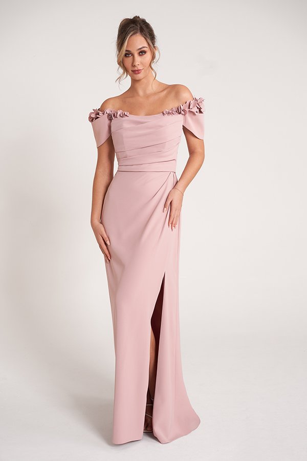 Elegant dusty rose mother of the bride gown featuring an off-the-shoulder neckline, draped bodice, floral shoulder embellishments, and a flattering floor-length silhouette with a chic side slit for formal occasions.
