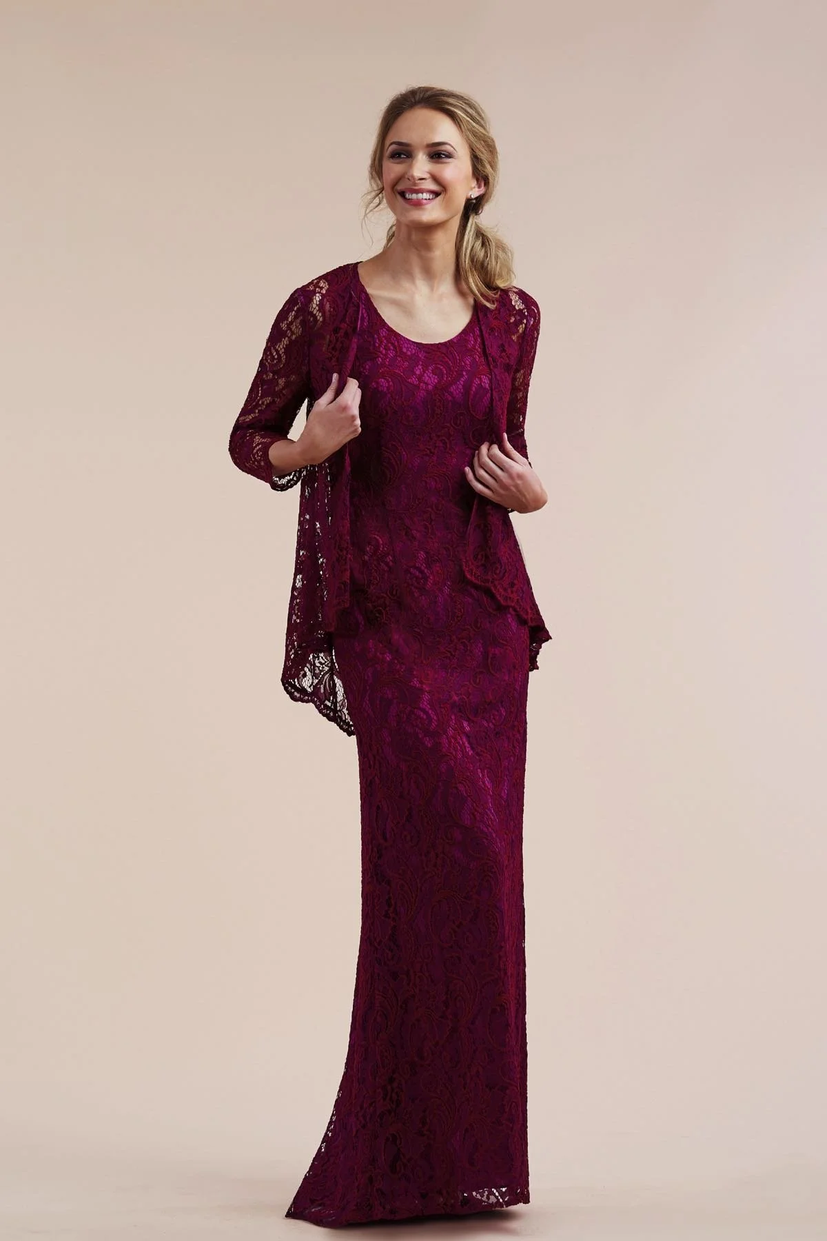 Woman modeling a berry mother of the bride lace column gown featuring a sleeveless scoop neckline and coordinating three-quarter sleeve lace jacket for formal occasions.