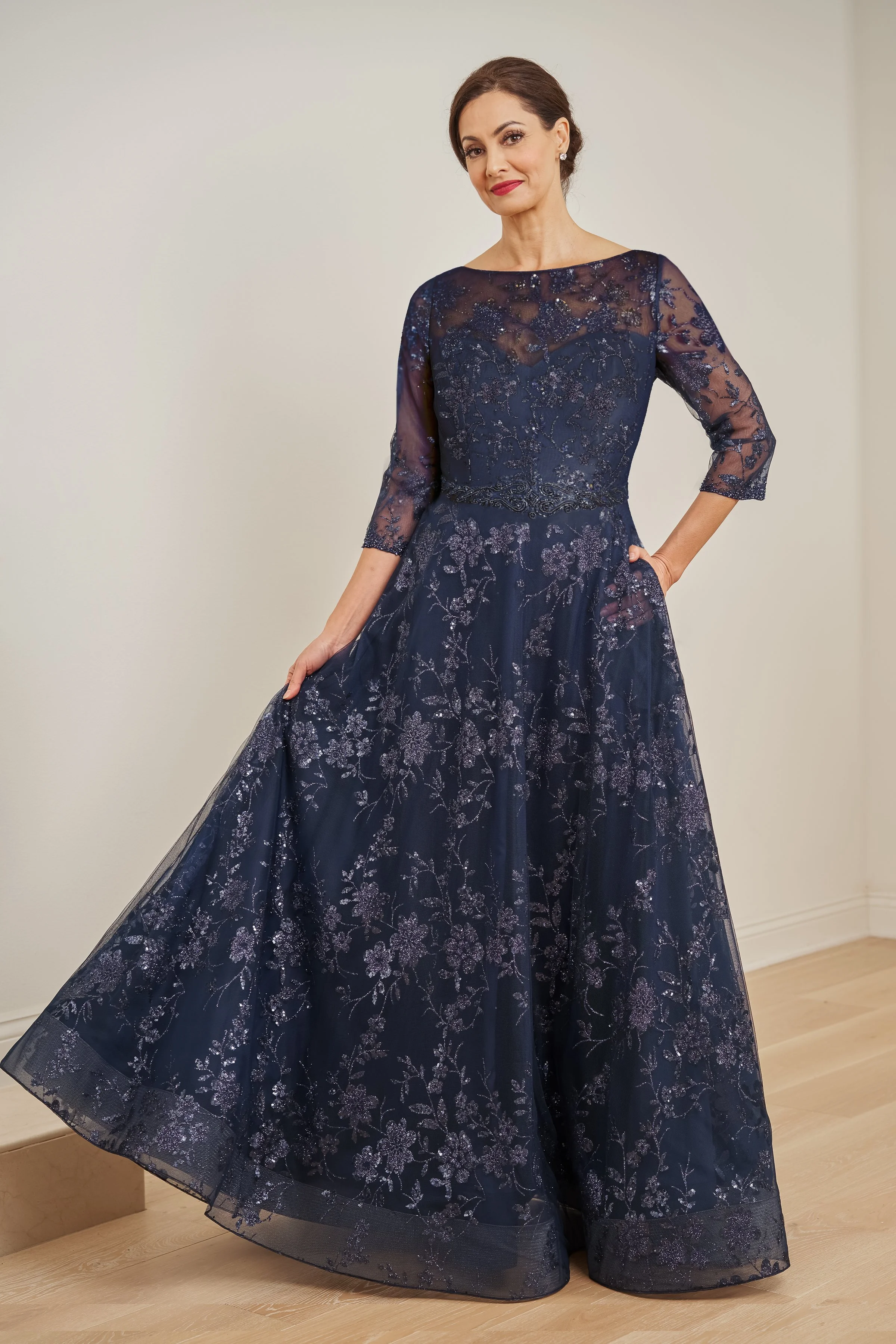 Front view of a navy mother of the bride gown with an illusion bateau neckline, sheer three-quarter sleeves, glitter floral embroidery, embellished waist detail, and a flowing A-line skirt for weddings and formal events.