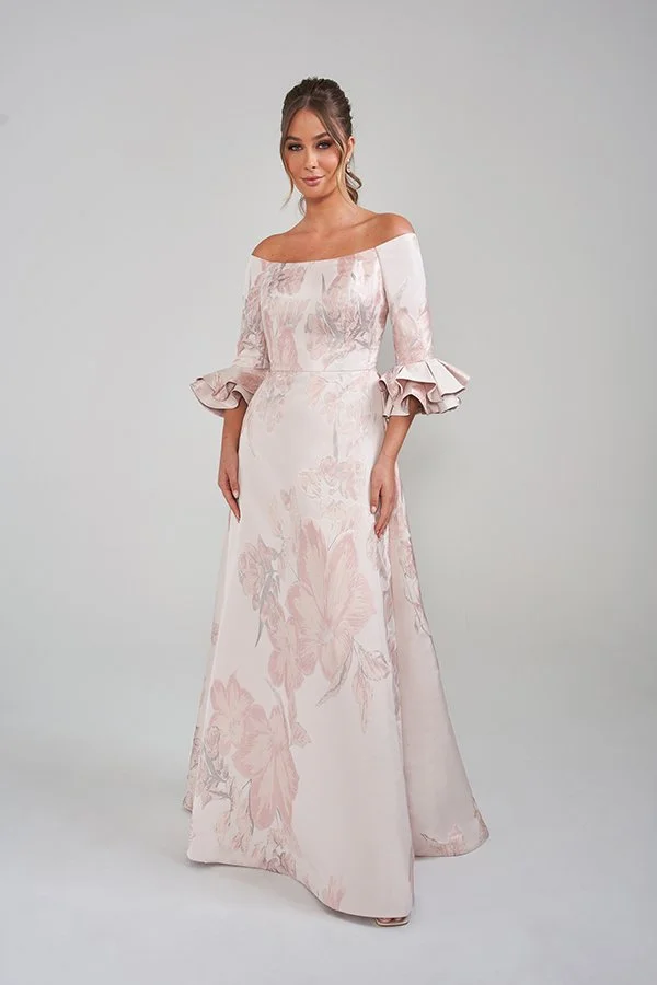 Elegant blush mother of the bride gown featuring an off-the-shoulder neckline, soft floral print fabric, three-quarter sleeves with statement ruffle cuffs, and a flattering floor-length A-line silhouette for formal occasions.