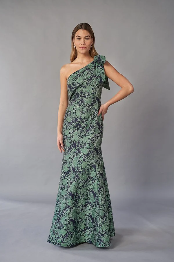 Front view of an elegant green and navy mother of the bride gown with a one-shoulder neckline, jacquard fabric, statement shoulder bow, and flattering mermaid silhouette for formal occasions.